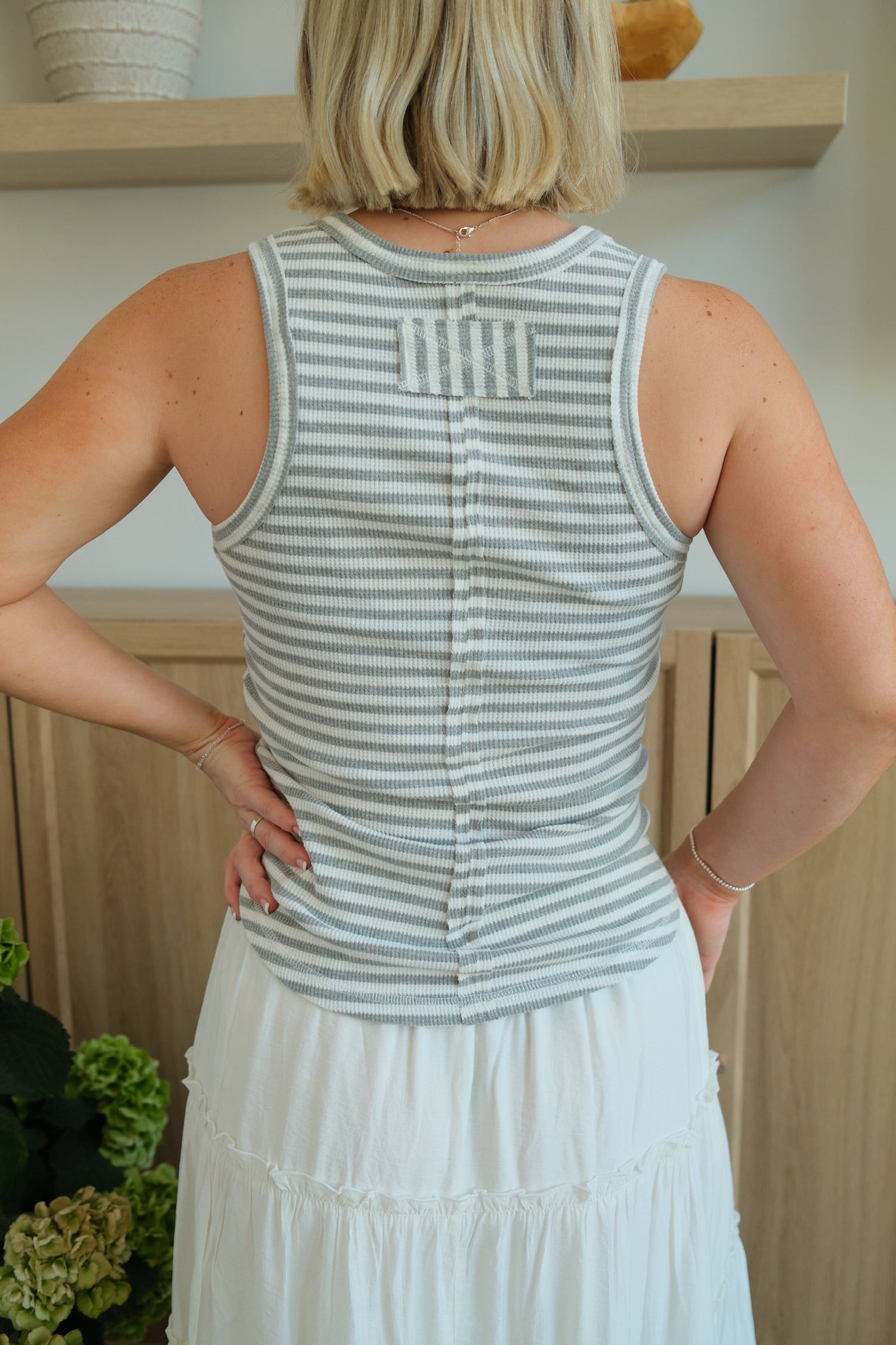 Person wearing a striped tank top and white skirt with a neutral background