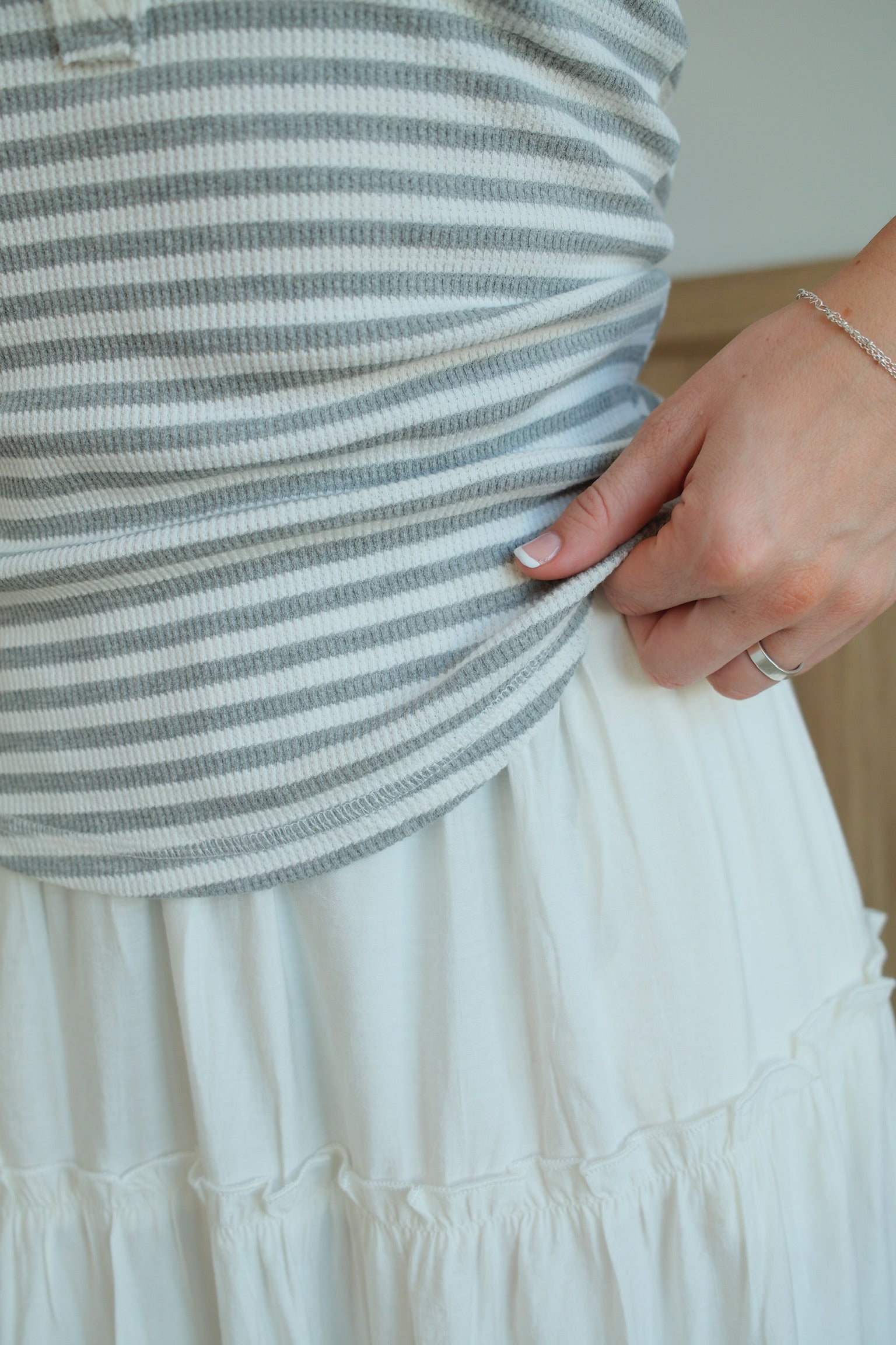 Person wearing a striped top and white skirt with a neutral background