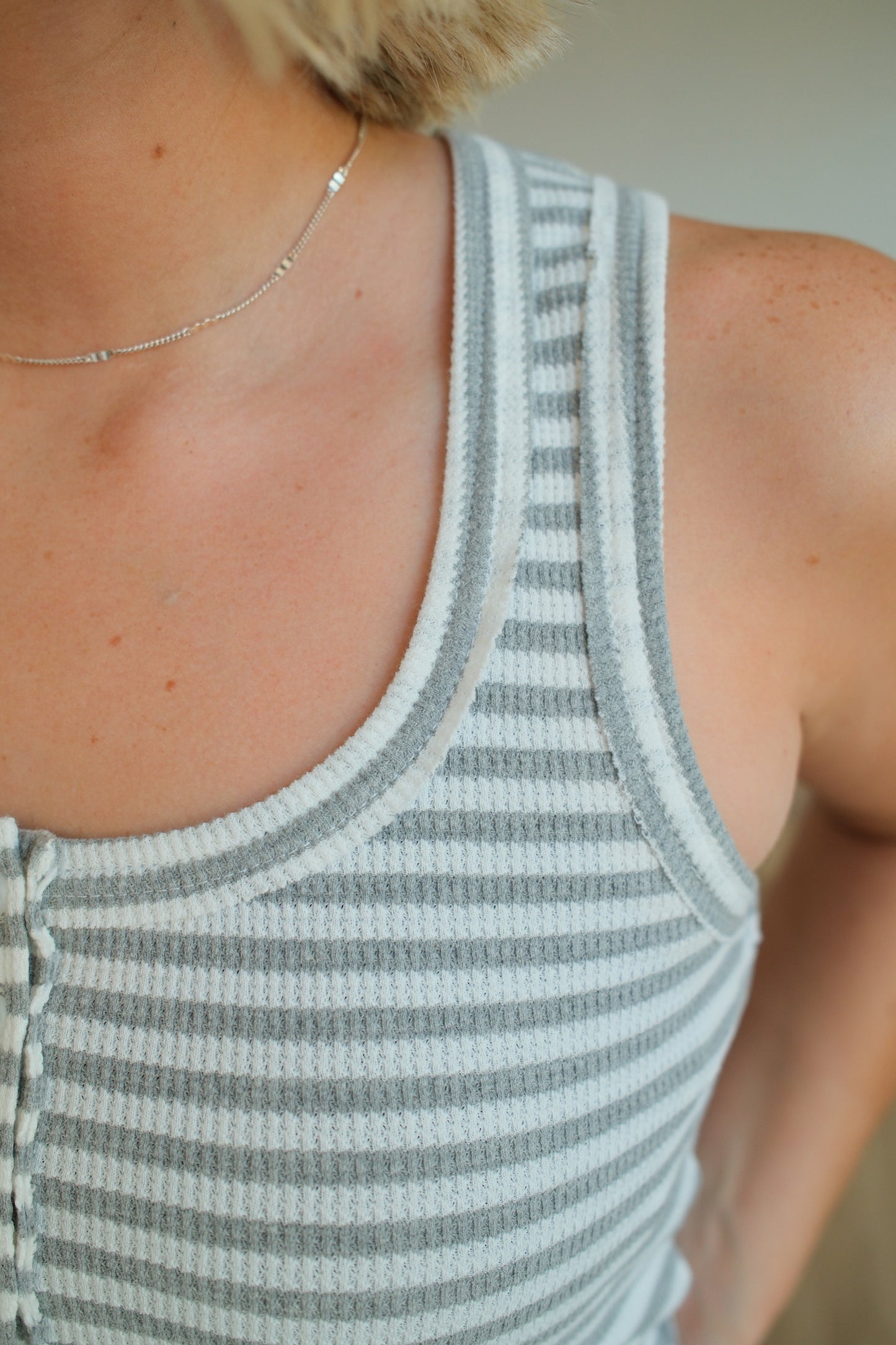 Person wearing a striped tank top with a neutral background